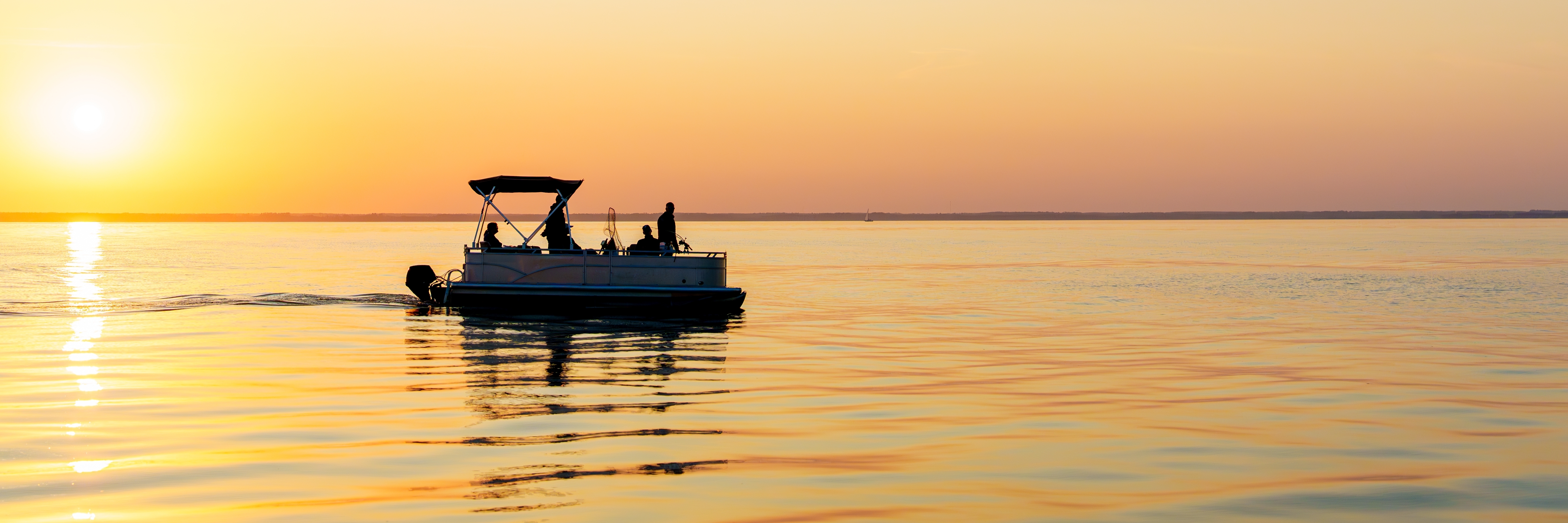 Sunset pontoon boat cruising across calm Lake of the Ozarks water with silhouetted passengers against a golden sky.