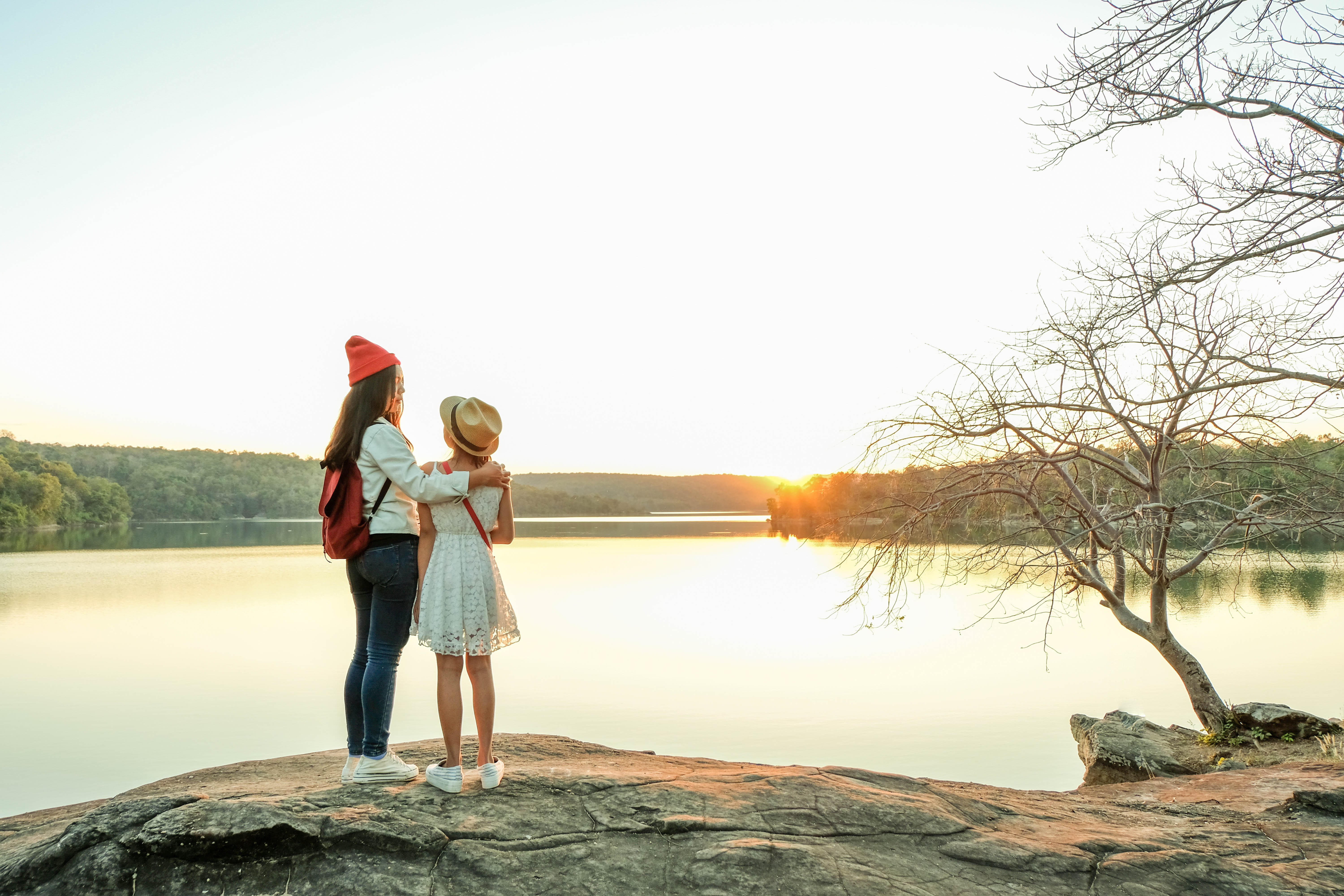 Two girls standing on a rocky overlook at Lake of the Ozarks in March, watching a calm sunset over the water in early spring.